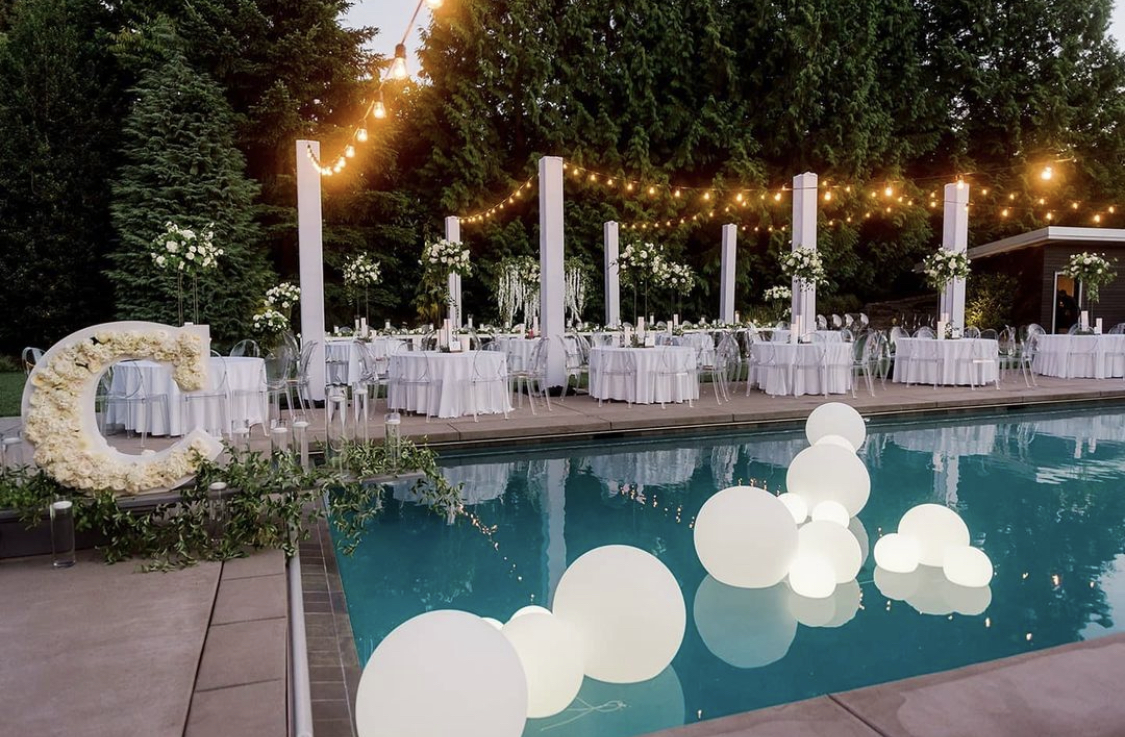 string lights hang from white columns around a pool with large floating globes